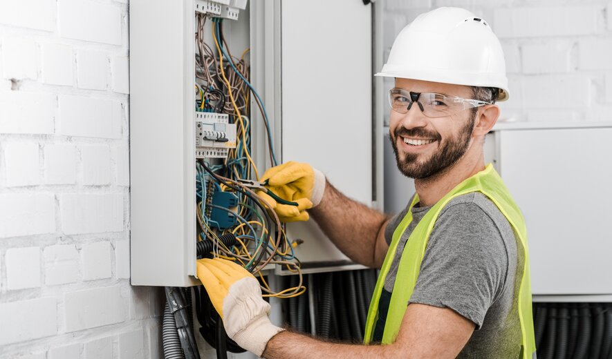 Ein Elektriker arbeitet lächelnd an einem offenen Schaltschrank voller Kabel.